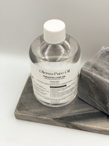 Zdjęcie produktowe, packshot krystalicznego oleju mineralnego Oliensa Pure Oil. Widok całej butelki na marmurowym kamieniu